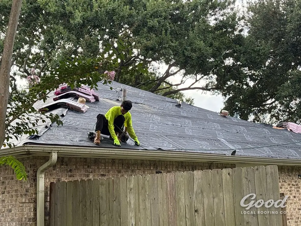 Roofer removing old shingles with exposed roof decking visible along the slope.