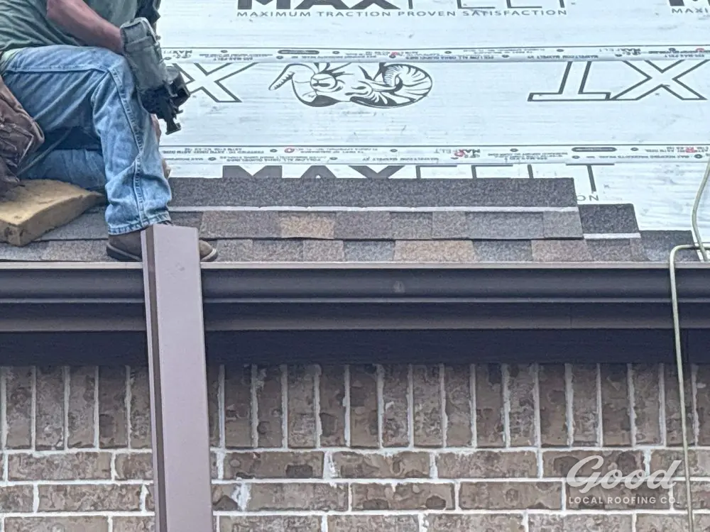 Roofer aligning a shingle course at the roof edge above a brick elevation.