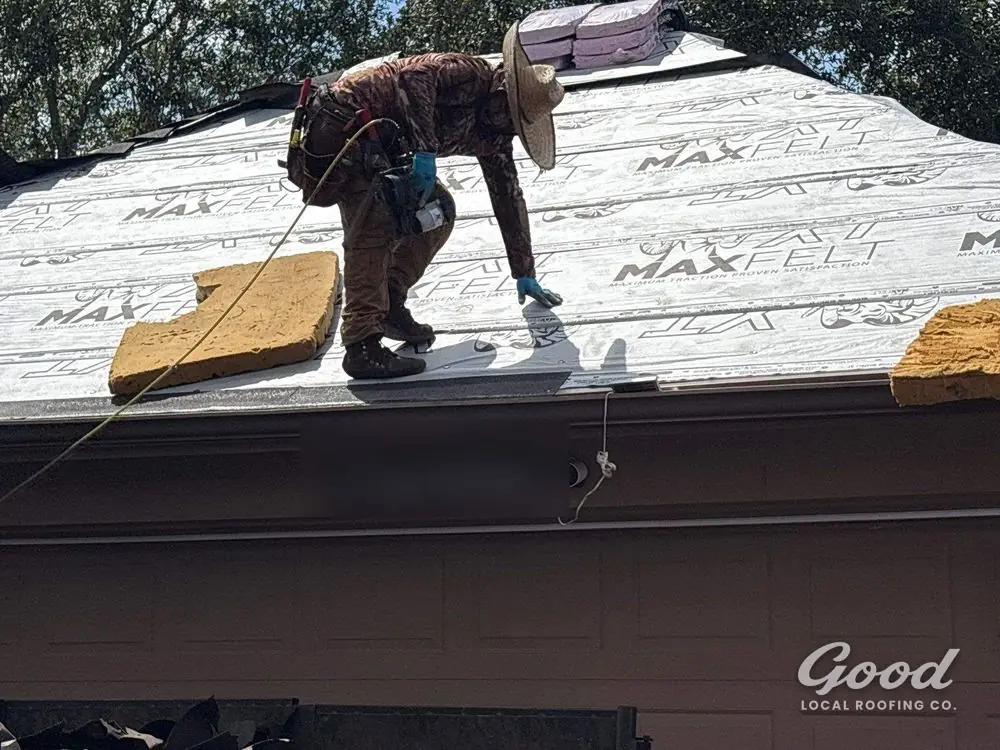 Roofer setting shingles on a garage roof plane over synthetic underlayment.