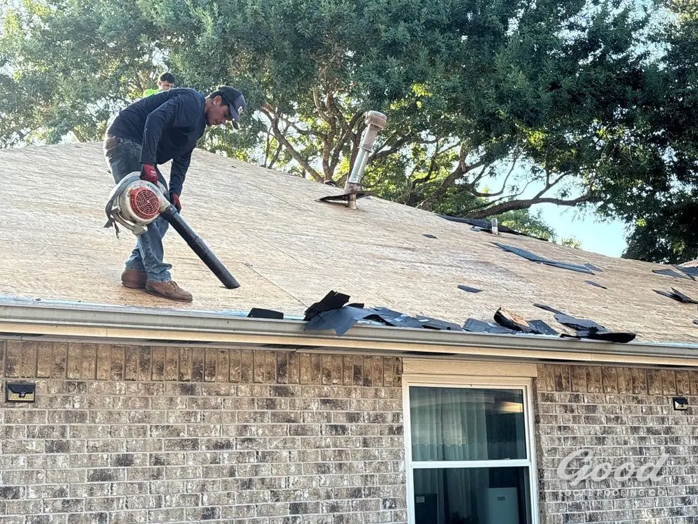 Roofer clearing debris from a roof surface with a blower during closeout.