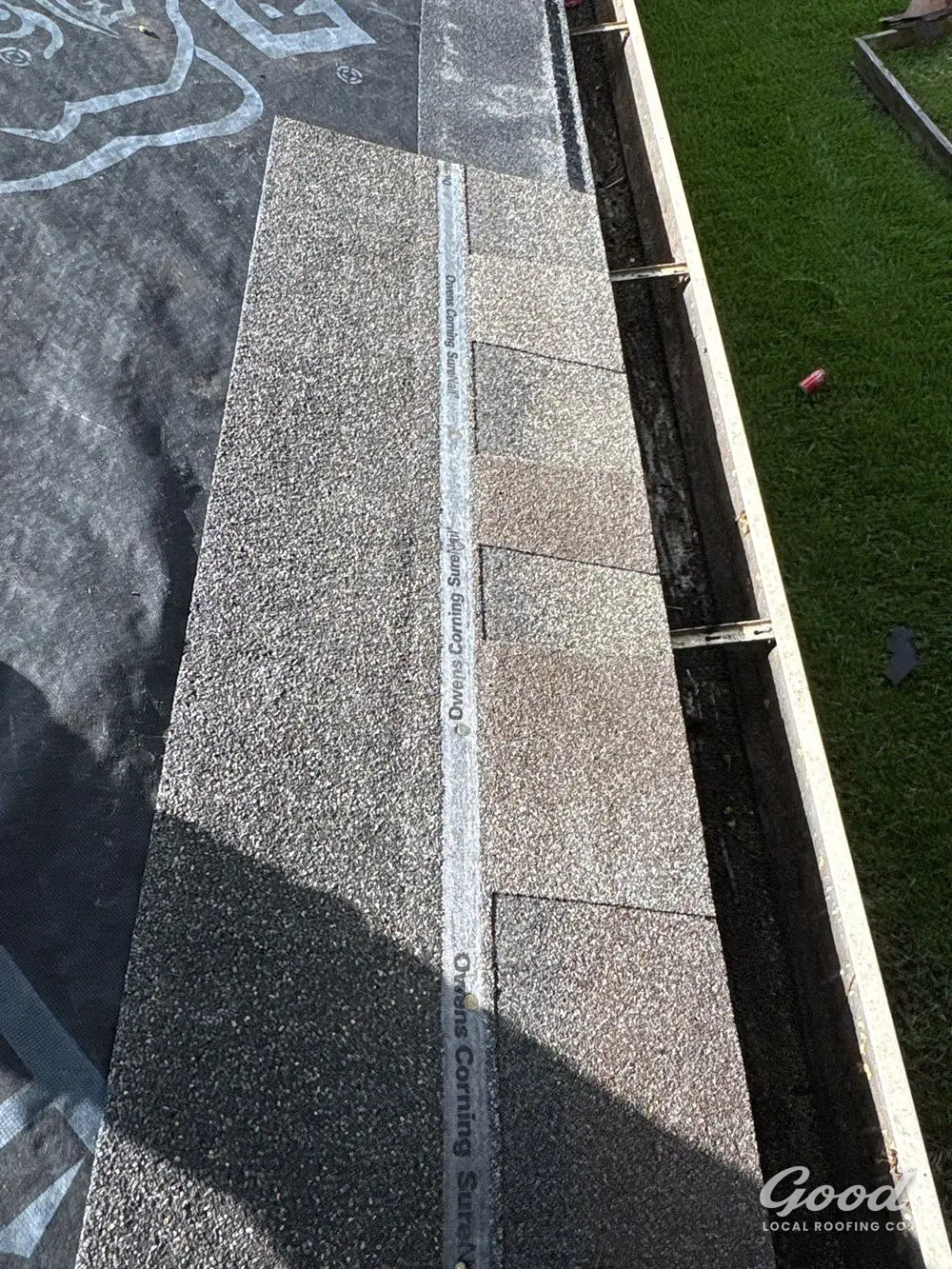 Detail of shingle edge, drip edge, and gutter line at a roof eave.