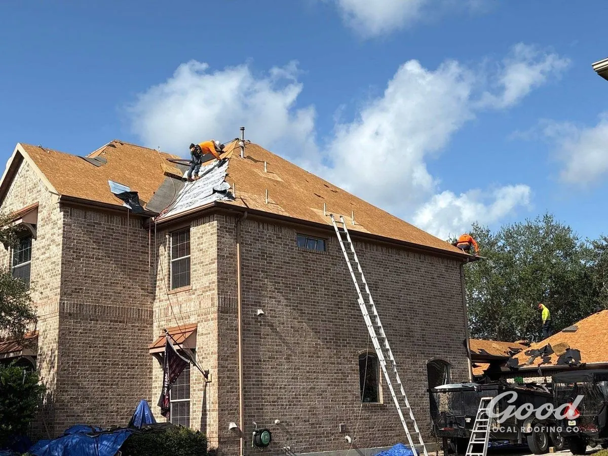 Roofer working over fresh roof decking on a two-story brick home.