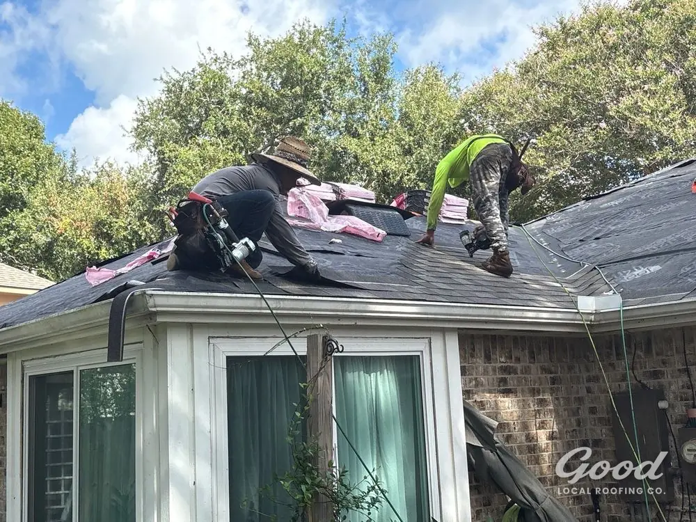 Two roofers working across a roof slope with bundles staged beside them.